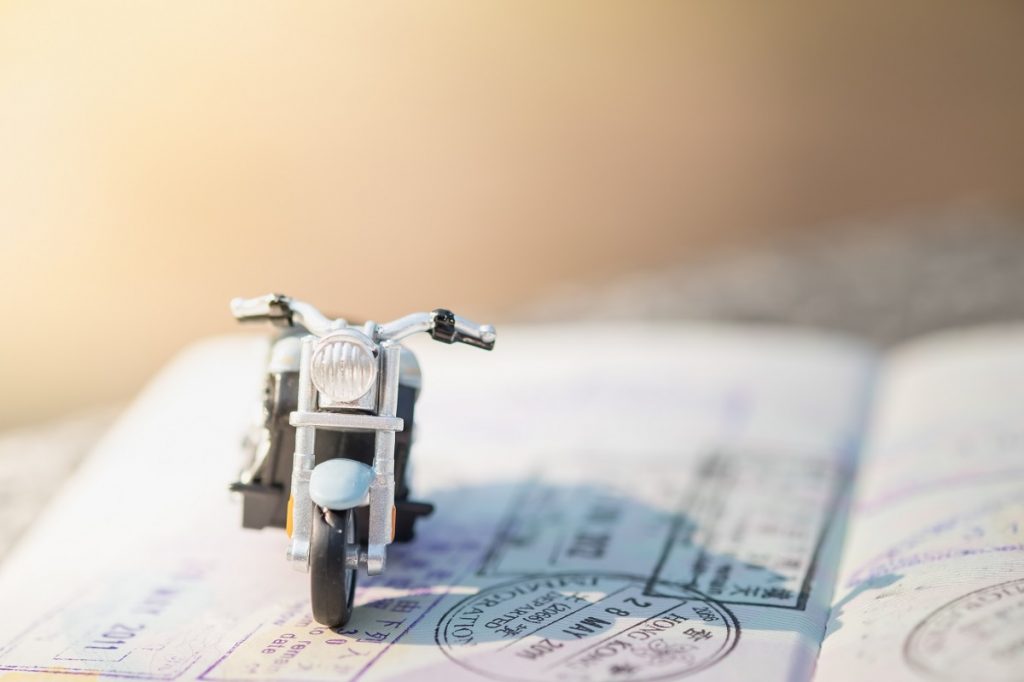 Travel Concept. Motorcycle miniature model figure on passport with immigration stamps under sunlight